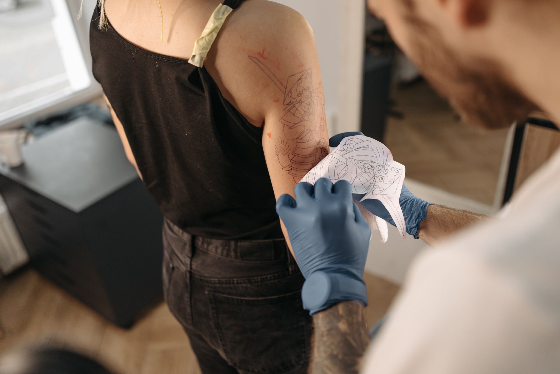 Tatuatore applica lo stencil sul braccio di una cliente
